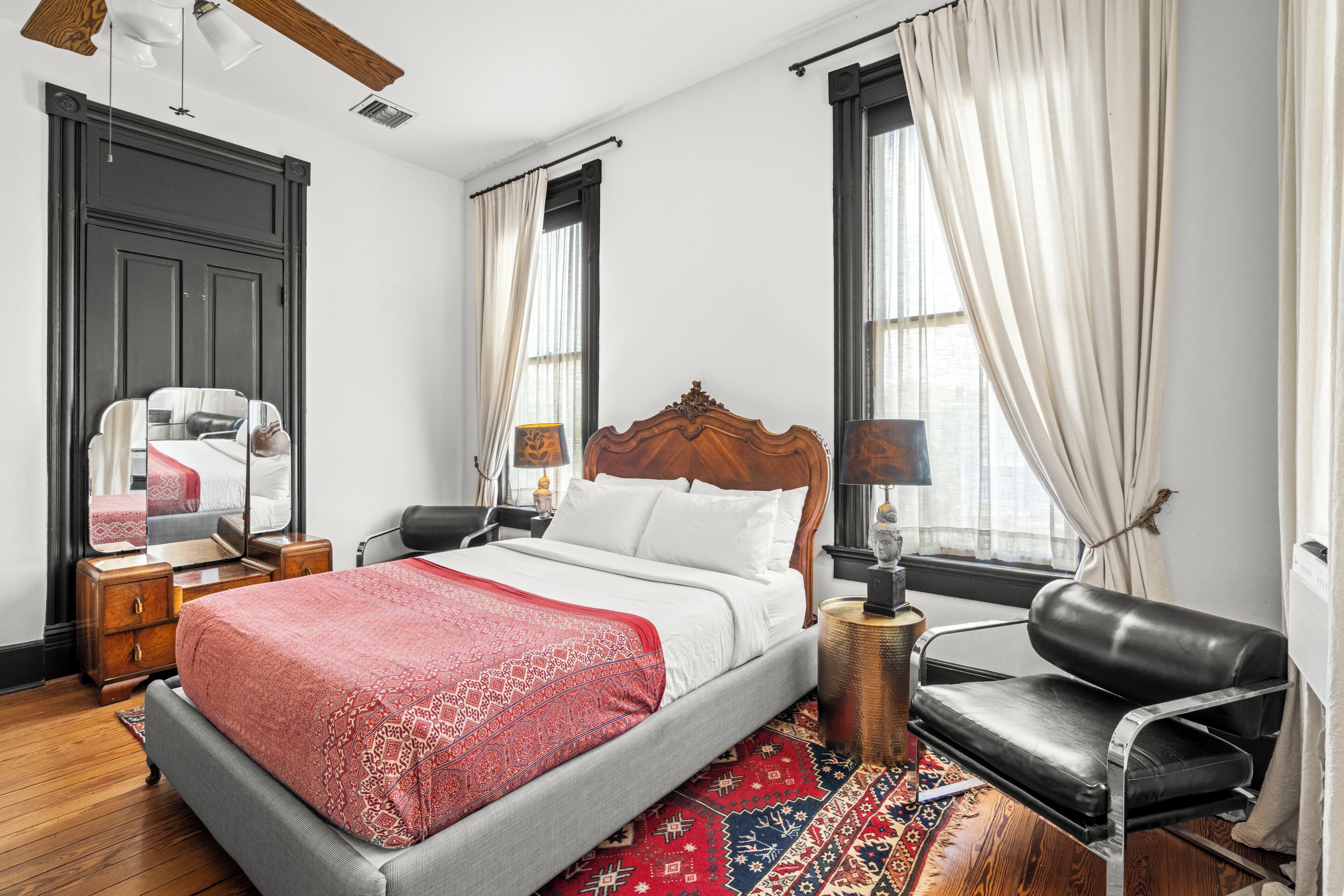 Une chambre d’hôtel avec un lit, une chaise, une table de chevet, une lampe et une fenêtre avec des rideaux.