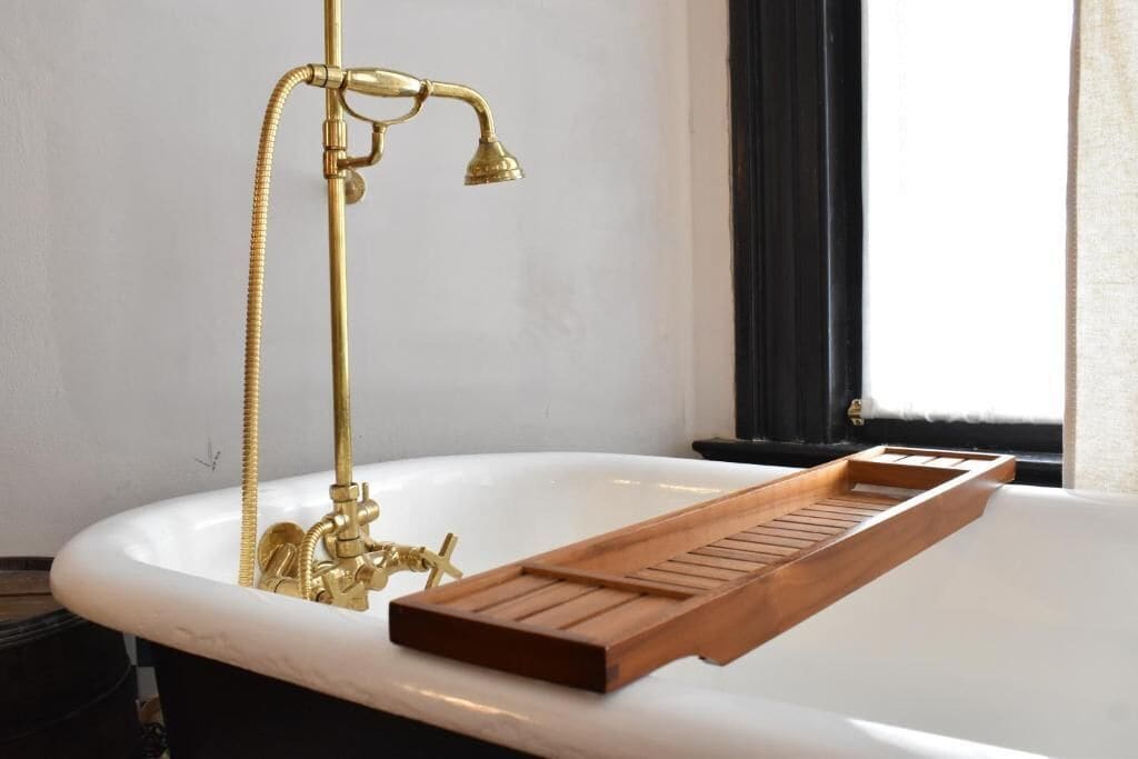 Une baignoire avec un plateau en bois, un robinet doré et un tuyau d’arrosage.