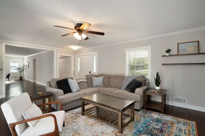 A living room with a sofa, coffee table, and a ceiling fan. There are two windows and a door. - Modern 3 Bedroom River Retreat in Heart of Athens (Athens)