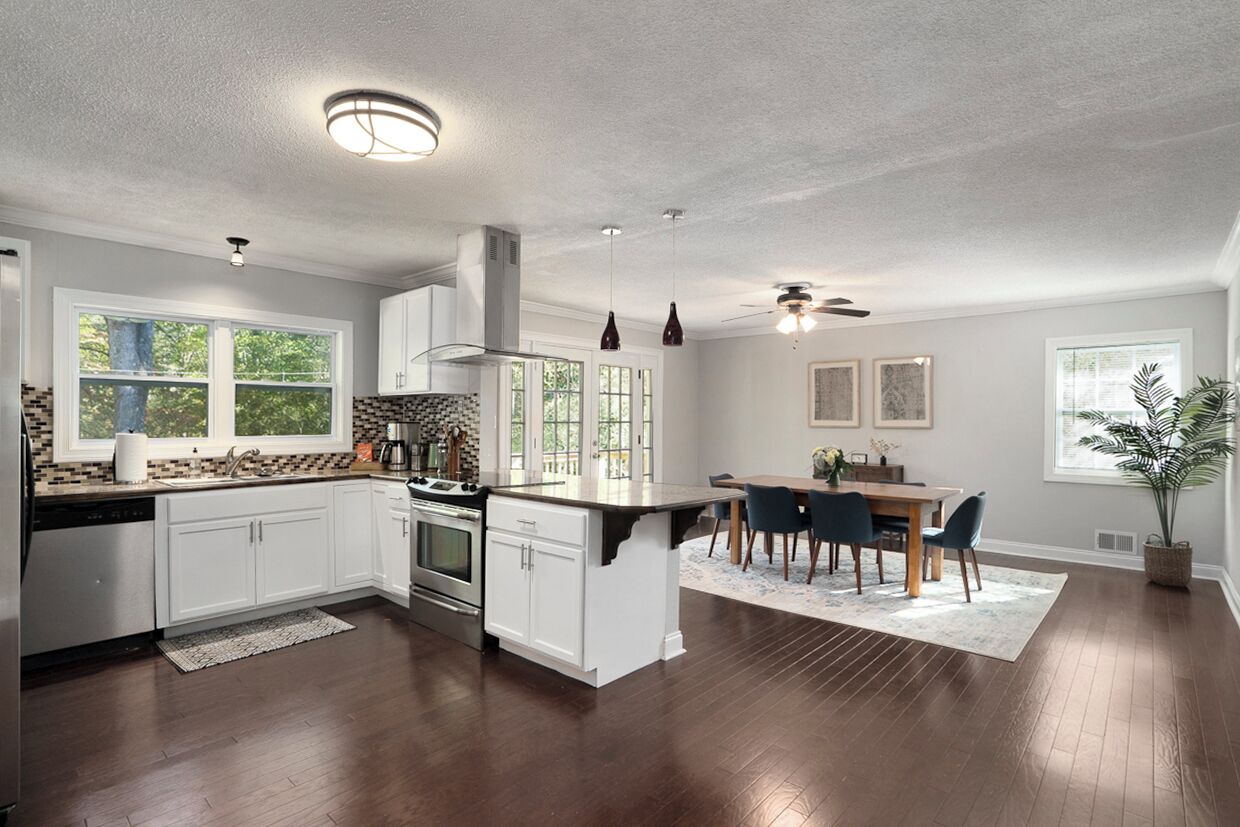 Una cocina moderna con armarios blancos, una isla central y una zona de comedor con mesa y sillas.