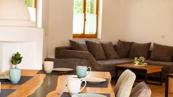 Een eetruimte met een houten tafel gedekt voor vier personen, een bank en een raam met uitzicht op groen.