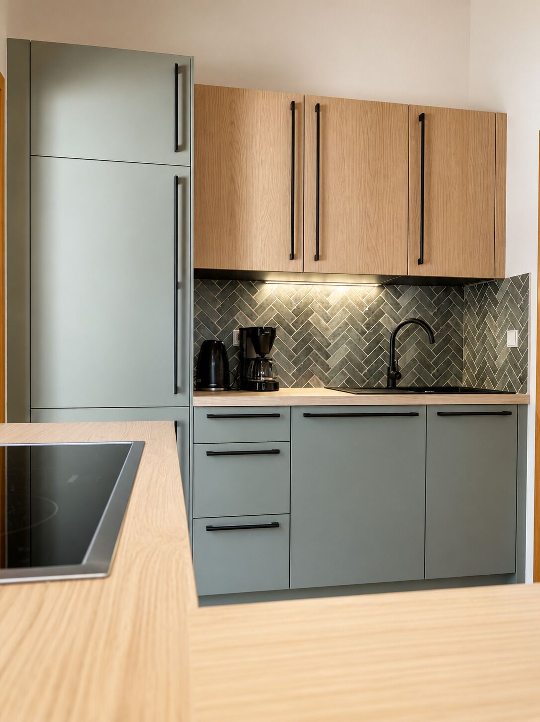 Une cuisine avec des meubles de couleur grise, un dosseret en motif chevrons et une cuisinière moderne.