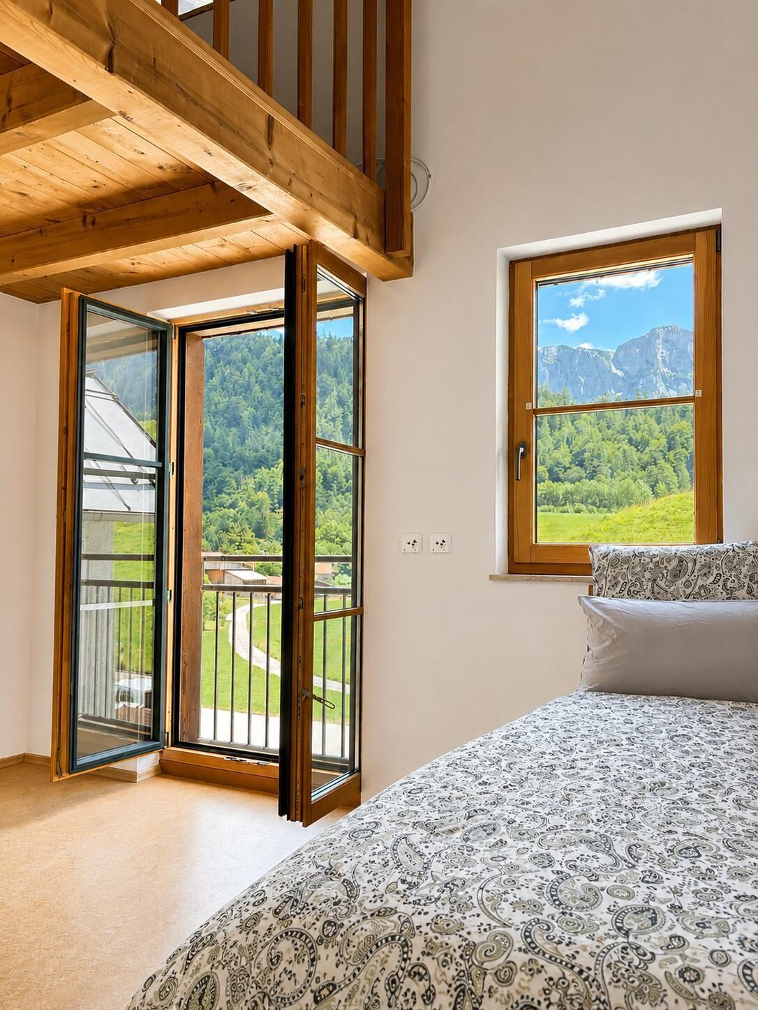 Une chambre à coucher avec un lit, une fenêtre donnant sur les montagnes et un balcon avec une balustrade.