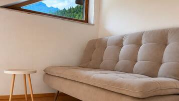 Een kamer met een bank, een tafeltje en een raam met uitzicht op bergen.