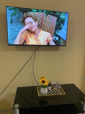Un televisor montado en la pared, con un tablero de ajedrez y un jarrón con girasoles debajo.