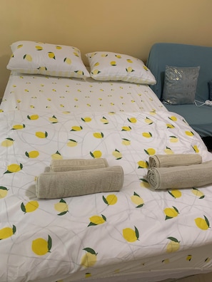A bed with a lemon pattern bedspread, two pillows, and two rolled towels. - Kabakum Beach Pool Studio Sea & Sun Escape (Varna)