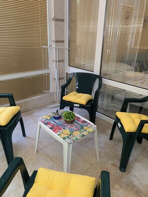 A room with a tiled floor, a table with a floral tablecloth, two chairs with yellow cushions, and a window with blinds. - Kabakum Beach Pool Studio Sea & Sun Escape (Varna)