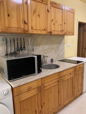 A kitchen with wooden cabinets, a microwave, a sink, and a stove. - Kabakum Beach Pool Studio Sea & Sun Escape (Varna)