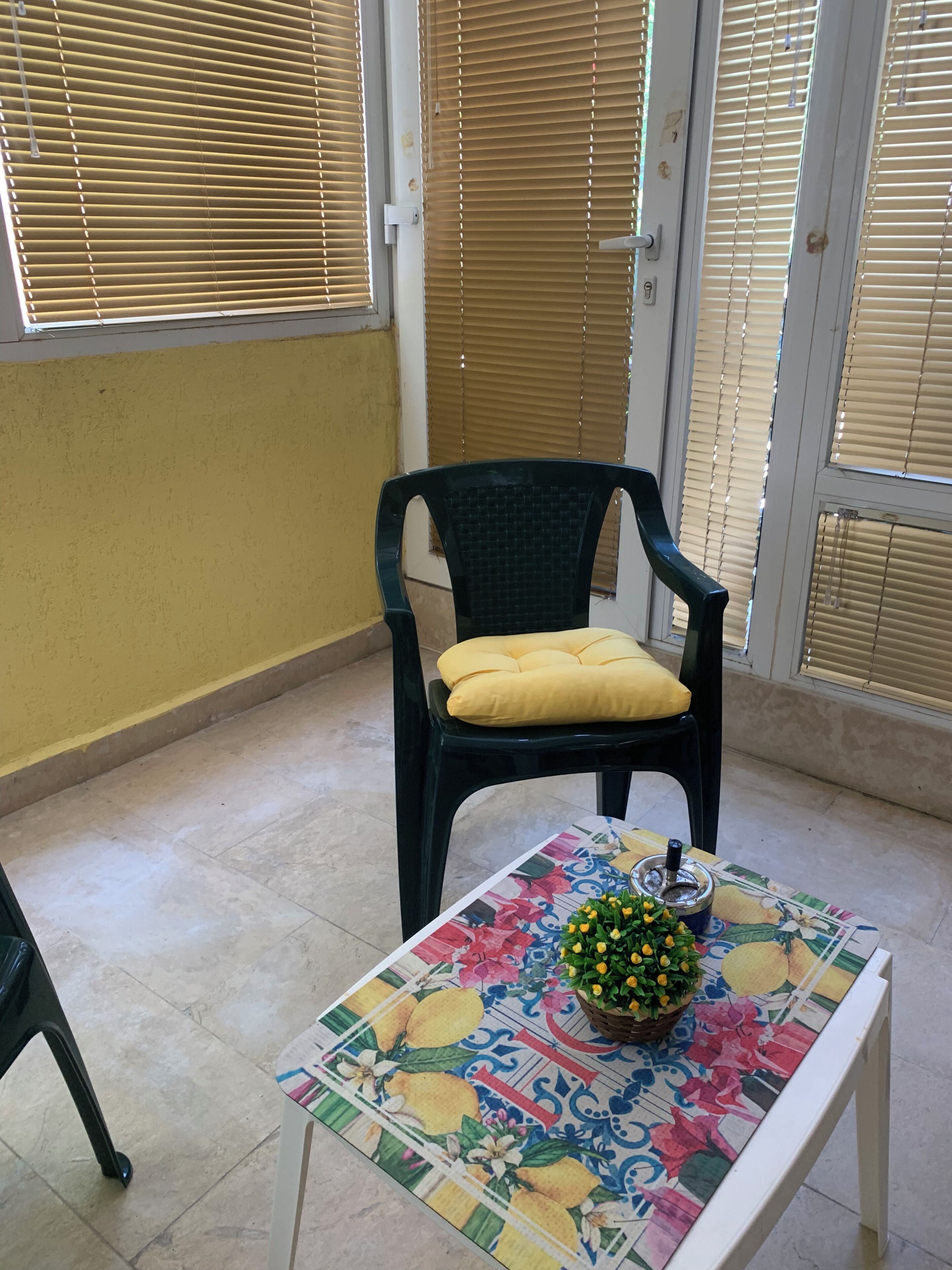 Ein Zimmer mit einem Stuhl, einem Tisch mit floraler Tischdecke und einem Fenster mit Jalousien.