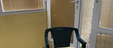 A room with a chair, a table with a floral tablecloth, and a window with blinds.