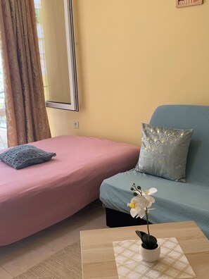 A room with a bed, a sofa, a small table with a plant, and a window with curtains. - Kabakum Beach Pool Studio Sea & Sun Escape (Varna)