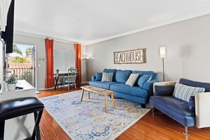 A living room with a blue sofa, a coffee table, and a rug. - Relaxing 2BR 2BA Steps to Beach, Shops, Dining (San Diego)