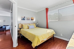 A bedroom with a bed, bedside table, lamp, and wall art. - Relaxing 2BR 2BA Steps to Beach, Shops, Dining (San Diego)