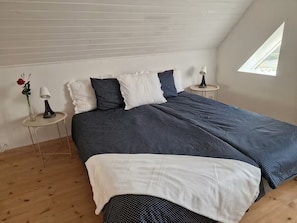 A bedroom with a bed, two bedside tables, a window, and a wooden floor.