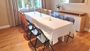 En spiseplads med et bord dækket til fire personer, stole, et vindue med gardiner og et spejl på væggen.