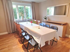 A dining area with a table set for four, chairs, a window with curtains, and a mirror on the wall. - Lovely house with a garden and pool in Österlen – Villa Harmoni (Löderup)