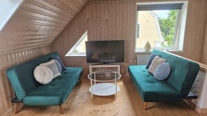 Et hyggeligt rum med to grønne sofaer, et fjernsyn og et glasbord.