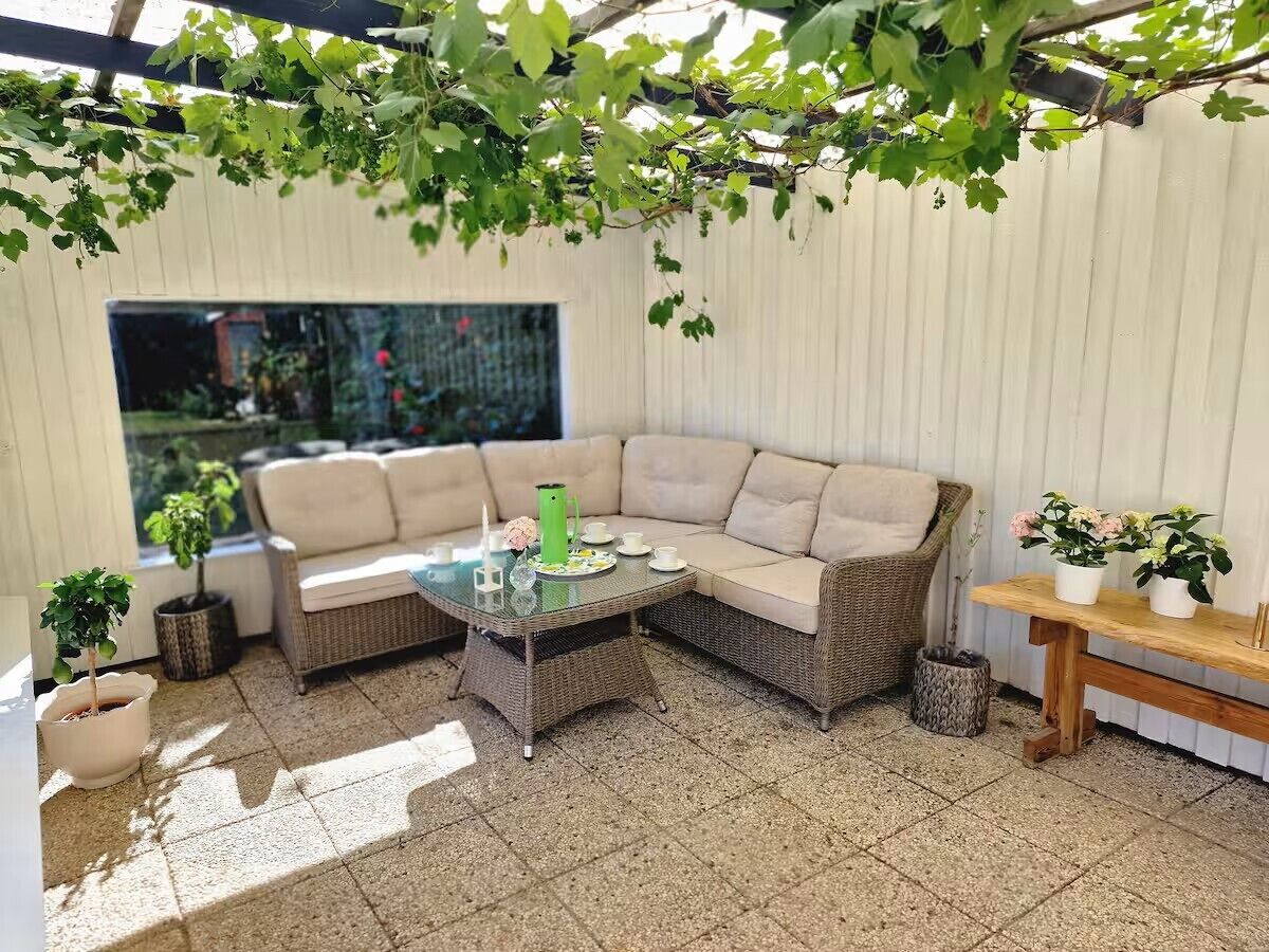 Un espace patio accueillant avec un canapé en osier, une table basse en verre et des plantes en pot.
