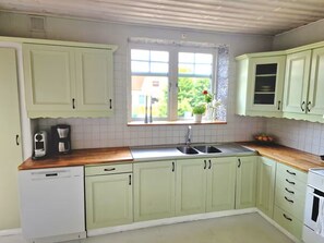 A kitchen with light green cabinets, a wooden countertop, a sink, and a window with a view of greenery. - Lovely house with a garden and pool in Österlen – Villa Harmoni (Löderup)