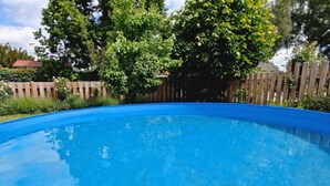 En lyseblå swimmingpool omgivet af et træhegn og frodig vegetation.