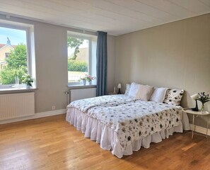 A bedroom with a large bed, a window with a view, a radiator, and a small table with a lamp. - Lovely house with a garden and pool in Österlen – Villa Harmoni (Löderup)