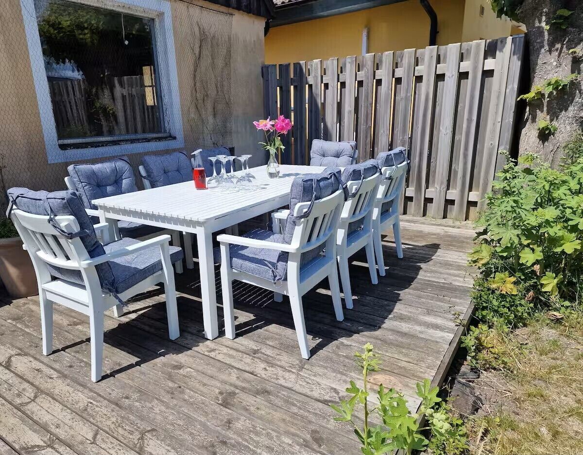 Un conjunto de comedor exterior blanco con sillas y mesa, rodeado por una terraza de madera y una valla de madera.