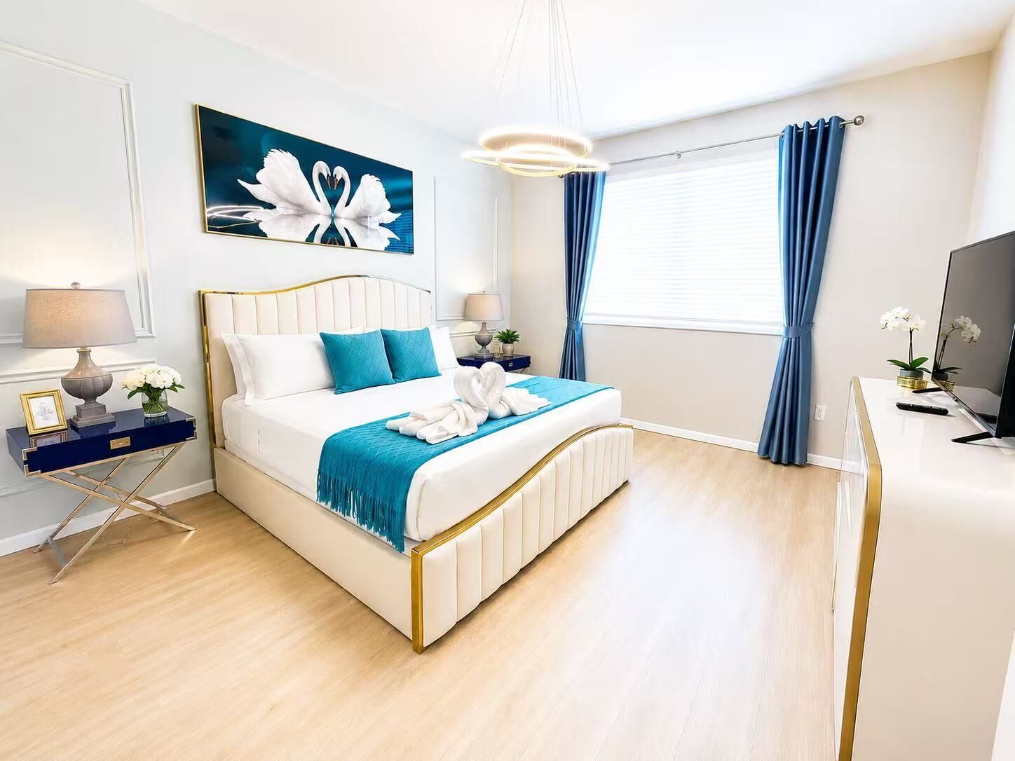 A modern hotel room with a bed, bedside tables, a TV, and a large window with curtains.
