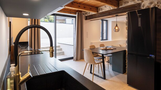A modern kitchen with a black refrigerator, a dining table with chairs, and a view of the outdoors through a glass door. - The Ostalet in Sampzon  (Sampzon)
