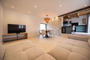 A modern living room with a flat-screen TV, a stone accent wall, and a dining area with chairs. - The Ostalet in Sampzon  (Sampzon)
