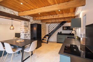 A modern kitchen with a stone accent wall, a black refrigerator, and a wooden staircase. - The Ostalet in Sampzon  (Sampzon)
