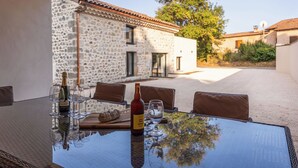 An outdoor dining area with a stone building in the background, a table with chairs, and a bottle of wine. - The Ostalet in Sampzon  (Sampzon)