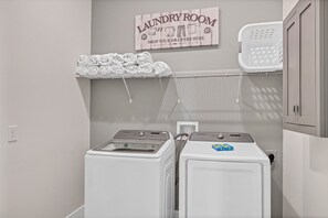 A laundry room with two washing machines, a wall-mounted sign, a shelf with folded towels, and a laundry basket. - Superb Home near Disney with Resort & Waterpark Access - 960JN (Kissimmee)