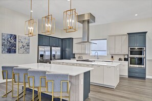 A modern kitchen with a central island, bar stools, stainless steel appliances, and pendant lighting. - Superb Home near Disney with Resort & Waterpark Access - 960JN (Kissimmee)