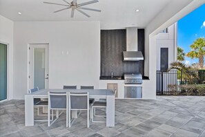 A modern outdoor kitchen with a dining table and chairs, a ceiling fan, and a herringbone-patterned backsplash. - Superb Home near Disney with Resort & Waterpark Access - 960JN (Kissimmee)