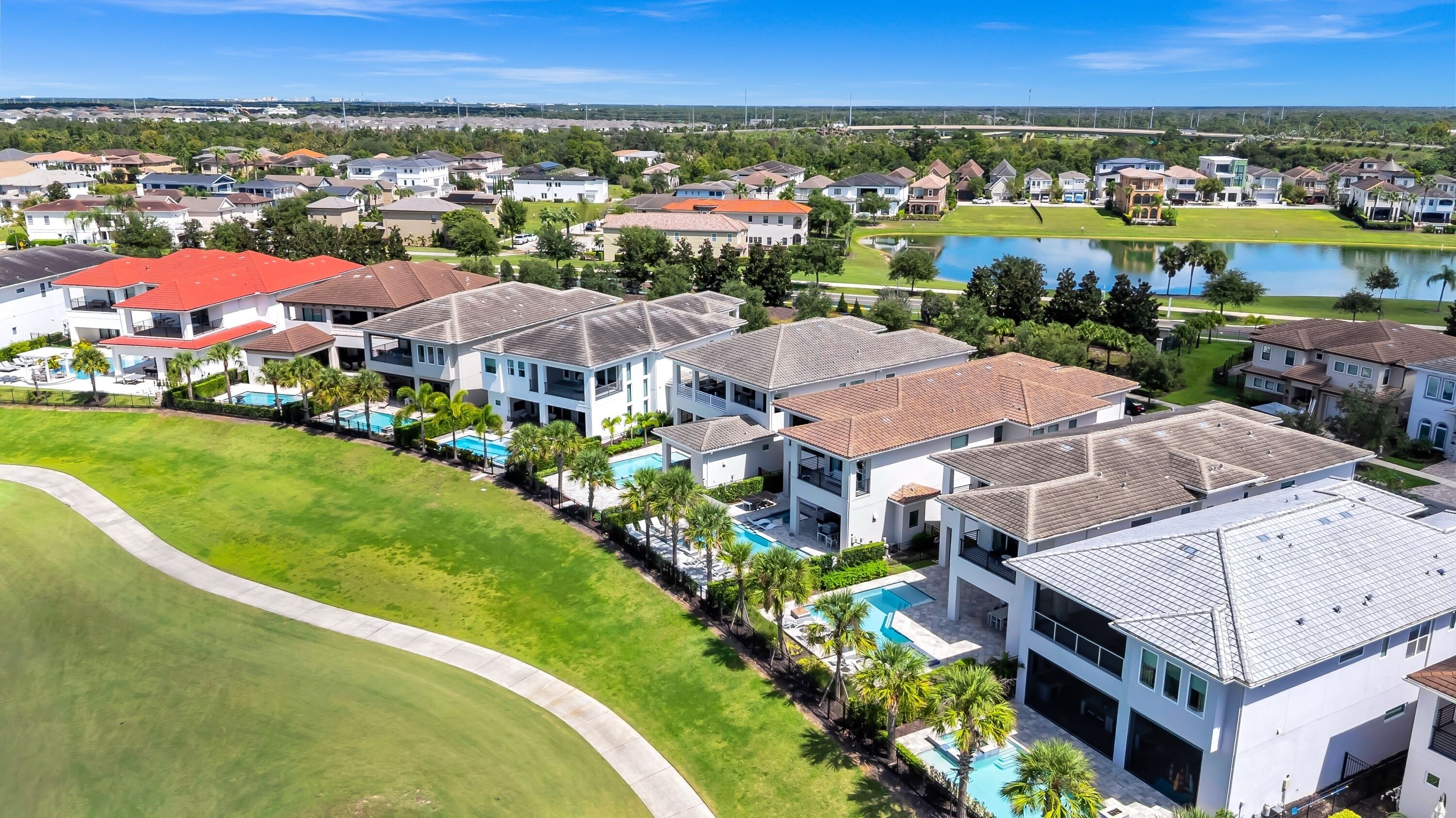 A residential area with modern houses, a swimming pool, and a golf course in the background.