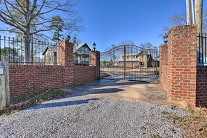 A gated driveway leading to a residential area with a brick wall, a metal gate, and a clear sky. - The Firefly House at Selah Manor- BIG Lake Views on all sides of the House! (Shelby)