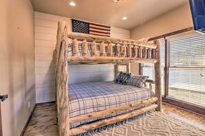 Ein Stockbett mit Holzrahmen und Karo-Bettwäsche, eine Flagge an der Wand und ein Fenster mit Jalousien.