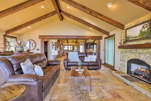 A spacious living room with leather sofas, a stone fireplace, and a view into the kitchen. - The Lighthouse at Selah Manor- BIG Lake Views on all sides of the House! (Shelby)