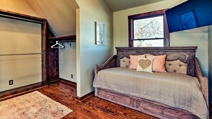 A bedroom with a bed, a window, a wooden floor, and a hanging clothes rack. - The Lighthouse at Selah Manor- BIG Lake Views on all sides of the House! (Shelby)