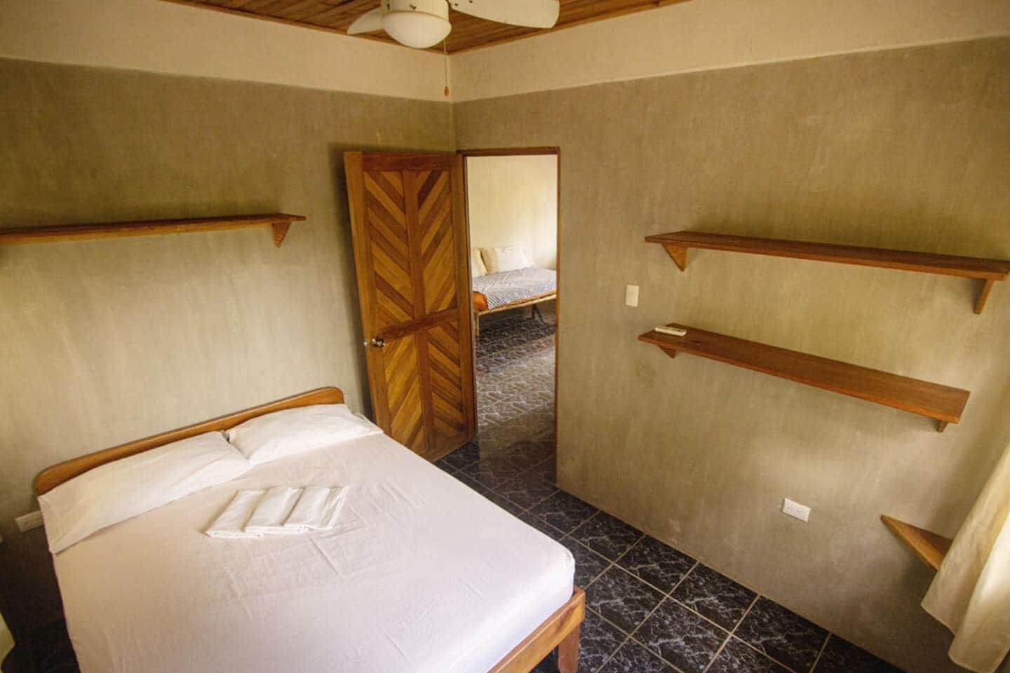 Un dormitorio con cama, cabecera de madera, una puerta y una pequeña estantería.