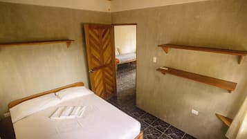 Un dormitorio con cama, cabecera de madera, una puerta y una pequeña estantería.