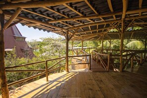 Eine Holzterrasse mit Metallgeländer, umgeben von üppiger Vegetation und einem Gebäude mit rotem Dach.