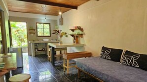 Una habitación con cama, un banco, una mesa y una zona de cocina.