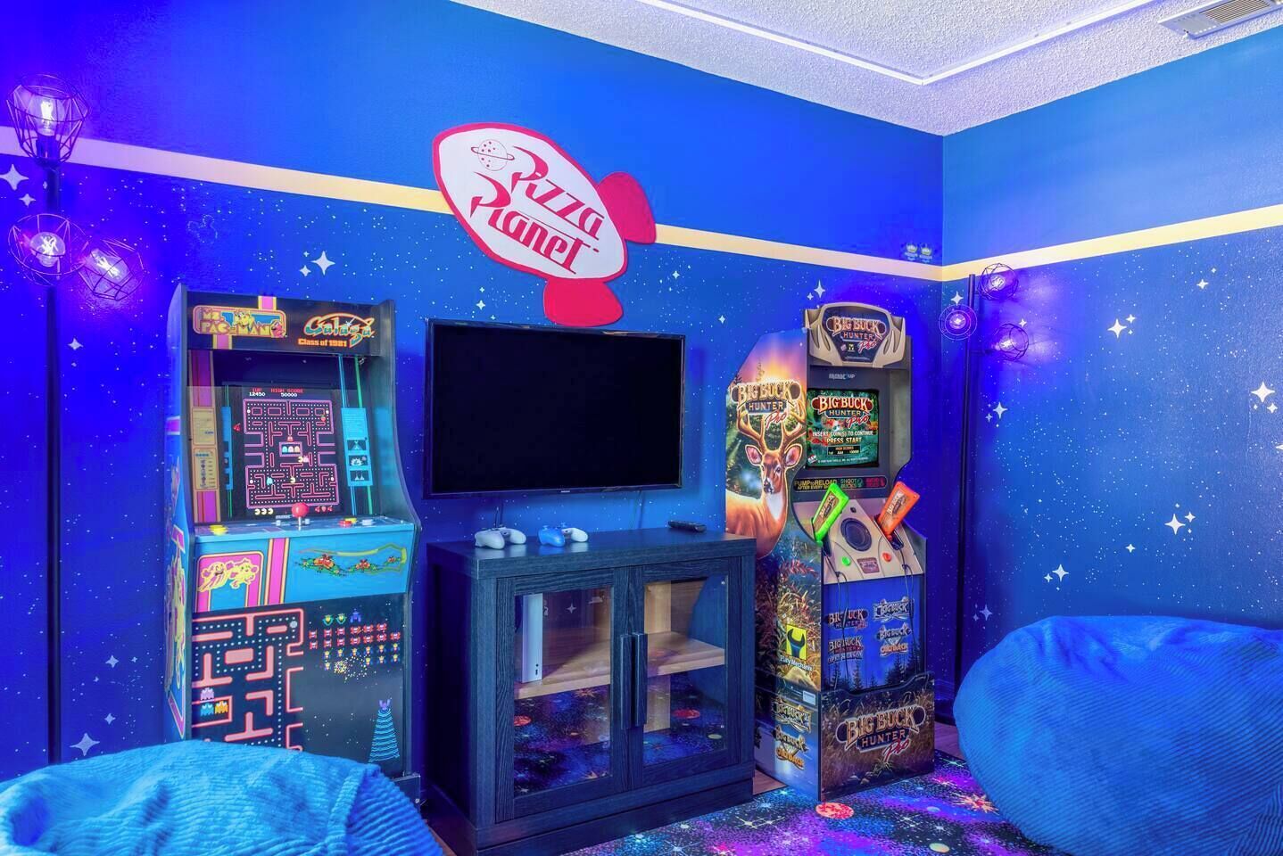 A room with a starry wall, a pizza-themed sign, arcade games, a TV, and a cabinet.