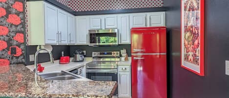 A kitchen with white cabinets, a red refrigerator, a microwave, and a stove.