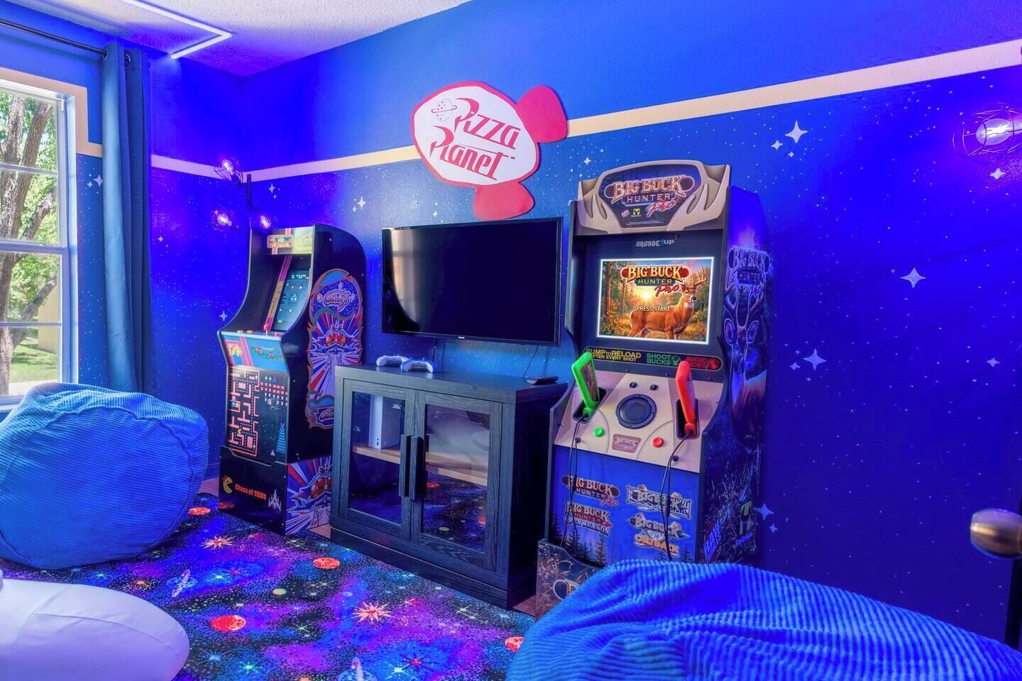 Une salle avec des jeux d’arcade, un téléviseur et une enseigne indiquant « Pizza Planet ».