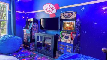 Une salle avec des jeux d’arcade, un téléviseur et une enseigne indiquant « Pizza Planet ».