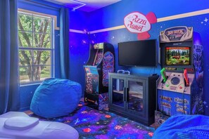 Ein Zimmer mit Fernseher, Spielautomaten, Sitzsack und Fenster mit Blick auf Bäume.