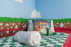 Ein Kinderzimmer mit kariertem Bettbezug, einem Kissen mit farbigem Muster und einer Wandmalerei.