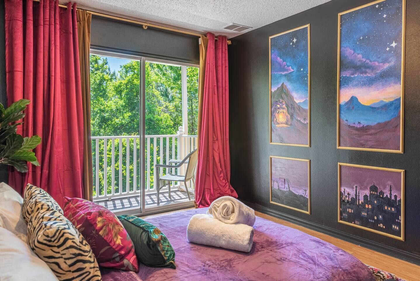 Une chambre avec un balcon, un lit doté de plusieurs oreillers et trois œuvres d’art encadrées accrochées au mur.